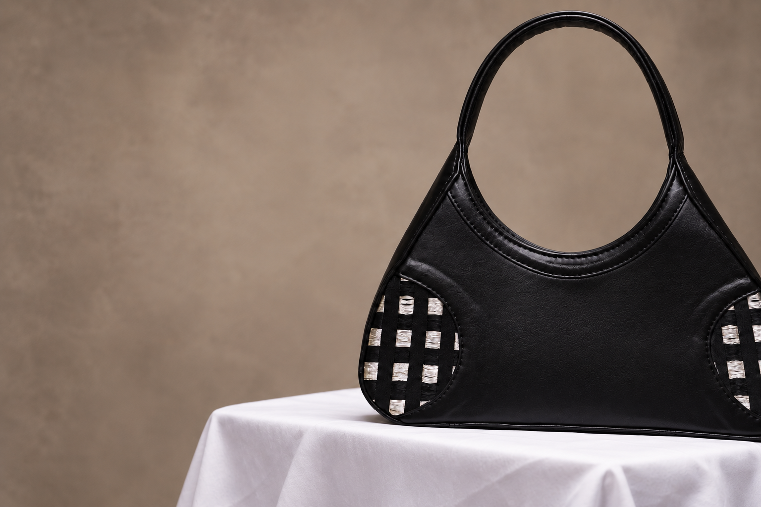 Black leather Orisun handbag with a looped handle and woven black-and-silver side panels, on white cloth.
